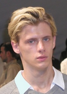 men layered haircut in blonde with long bangs pulled back
